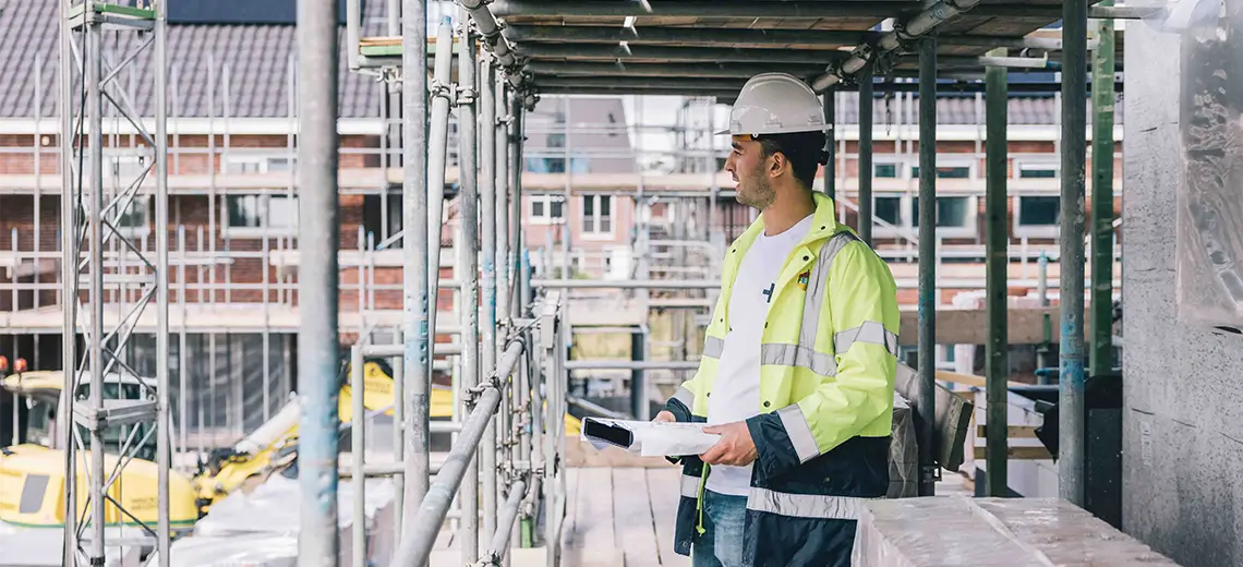 man met bouwhelm op stijgers in woningbouw